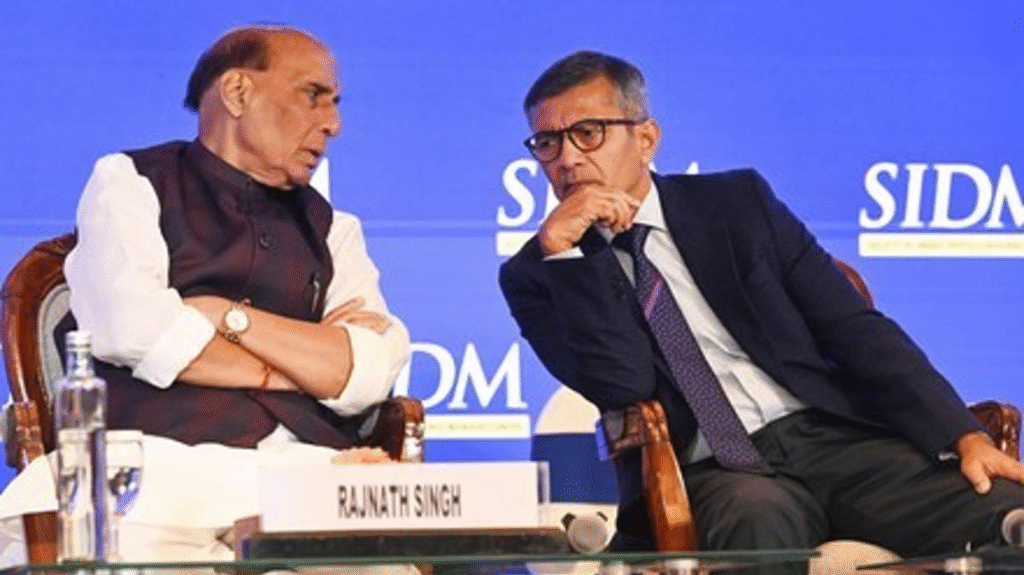 Defense minister Rajnath singh seated at a podium with officials during defense procurement news briefing.